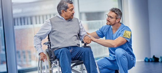 Pfleger spricht mit Mann im Rollstuhl